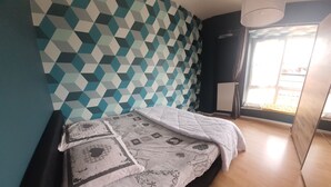 A bedroom with a geometric-patterned wall, a bed with patterned bedding, a radiator, and a window with curtains.