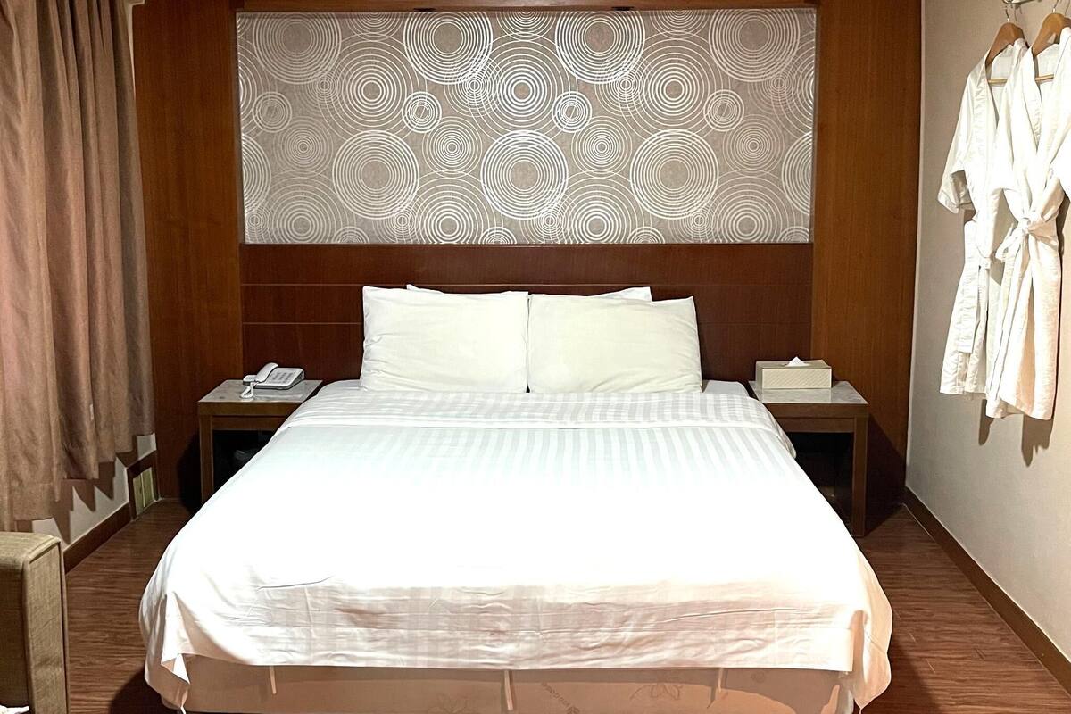 A hotel room with a large bed, two bedside tables, a telephone, and a robe hanging on the wall.