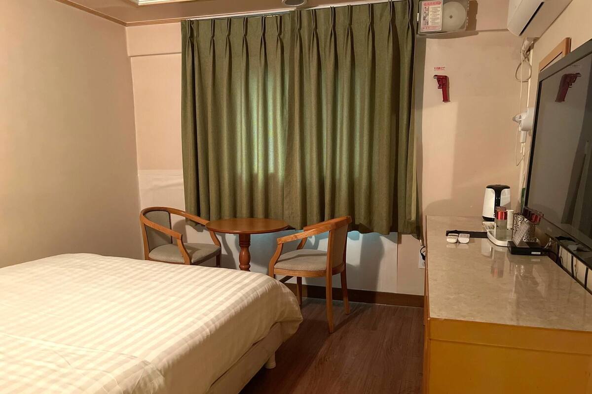 A hotel room with a bed, two wooden chairs, a small round table, a coffee maker, and a TV.