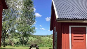 A red barn with a metal roof, a gravel path leading to a picnic table, and a view of green fields and trees in the background. - 4 Person Holiday Home in Ullared (Ullared)