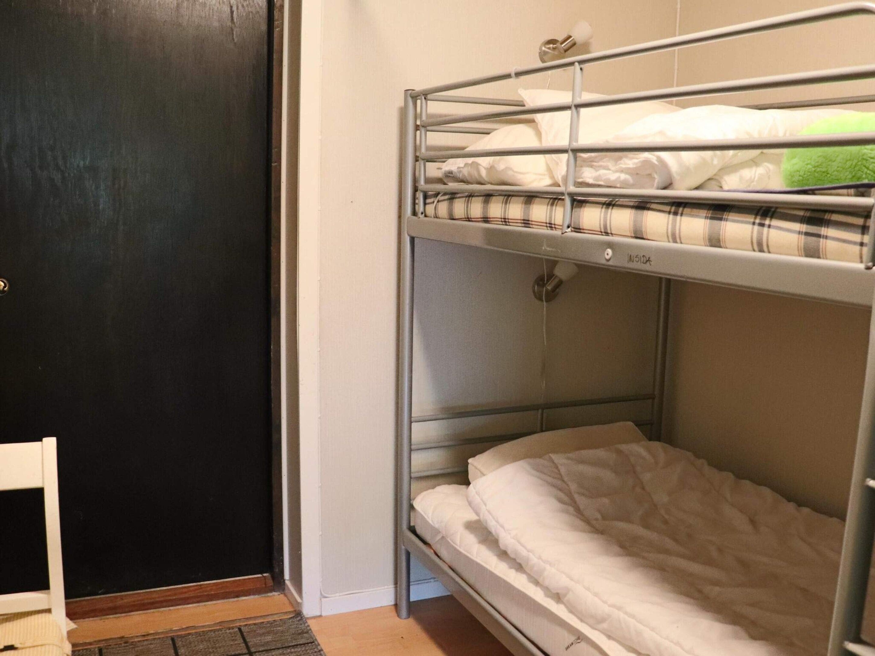 Una cama litera con estructura metálica, colchón blanco y manta escocesa.