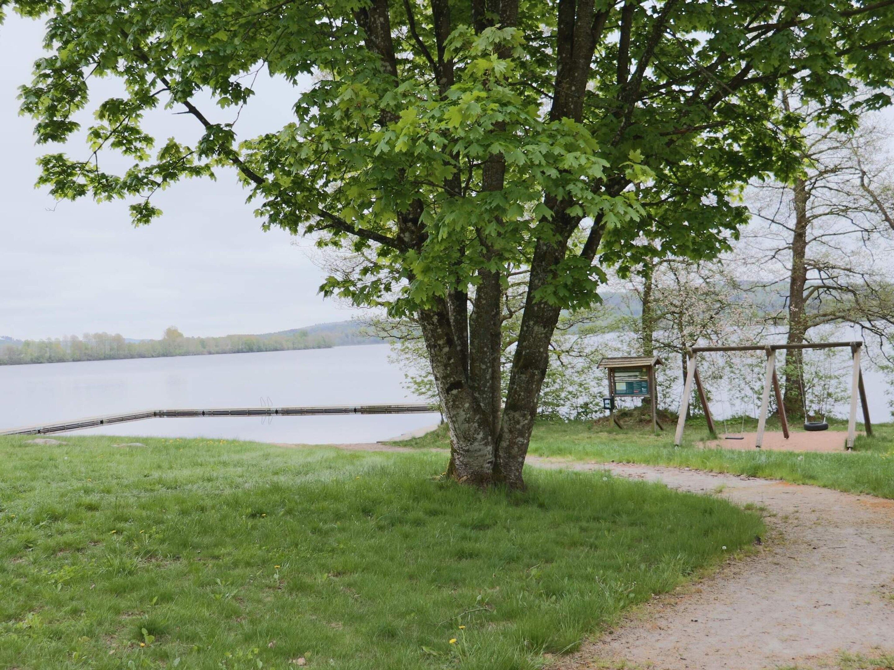 A lakeside park with a walking path, a swing set, and a small information board.