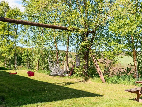 A grassy outdoor area with trees, a swing, a picnic table, and a red bucket. - 4 Person Holiday Home in Ullared (Ullared)