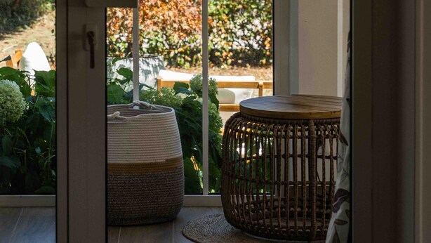 A room with a large window, a wicker chair, and a woven ottoman. - Villa Mariette, large charming villa with lake view, swimming pool and large garden (Doussard)