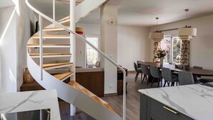 A modern kitchen with a marble countertop, a wooden staircase, and a dining area with a large table and chairs. - Villa Mariette, large charming villa with lake view, swimming pool and large garden (Doussard)