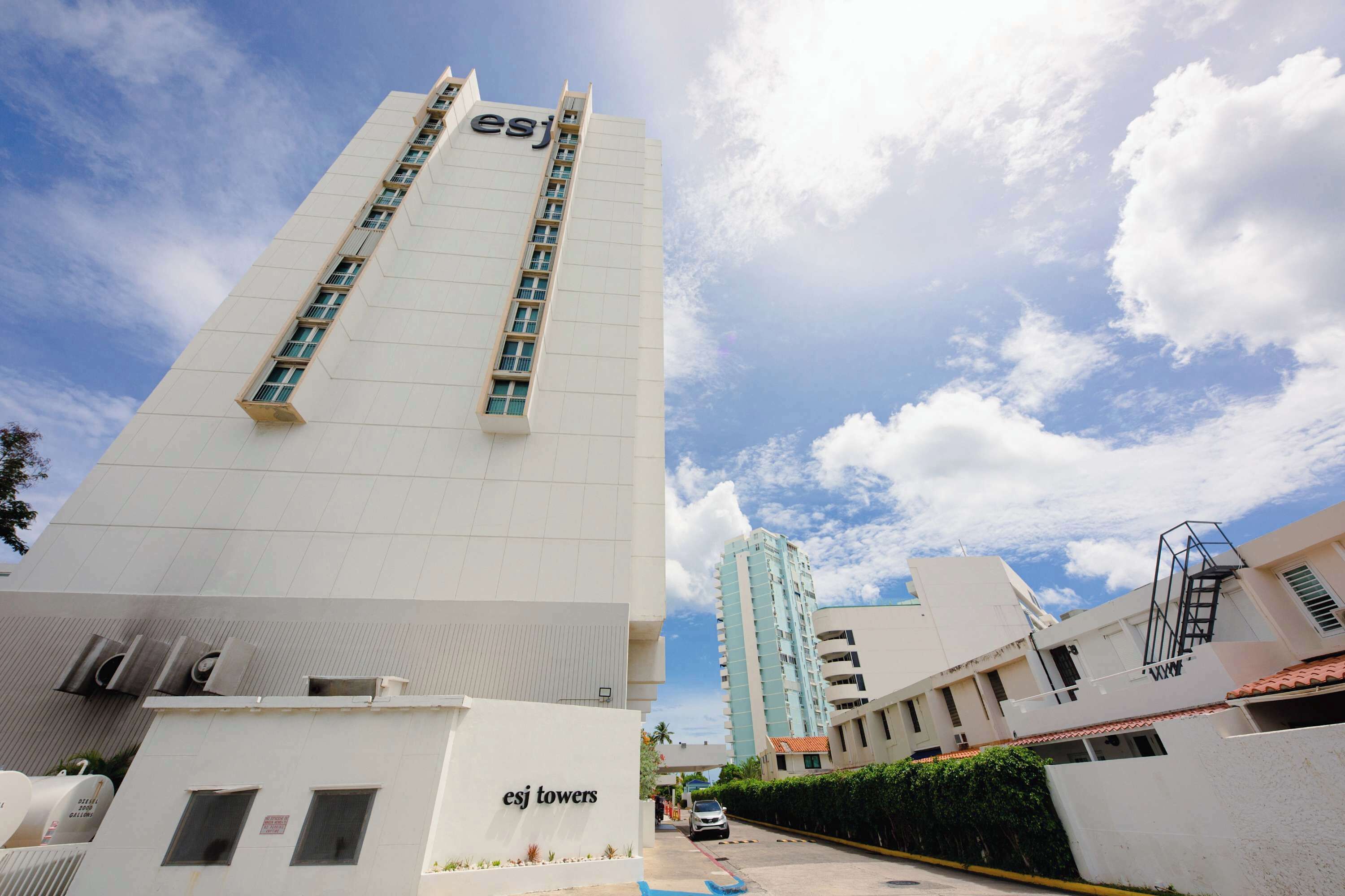 Un edificio alto y blanco con el rótulo 'esj towers' en su fachada, que presenta múltiples ventanas y un cielo despejado al fondo.
