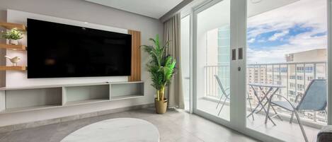 Een moderne woonkamer met een grote flatscreen televisie, een ronde marmeren tafel, een potplant en een balkon met buitenmeubilair.