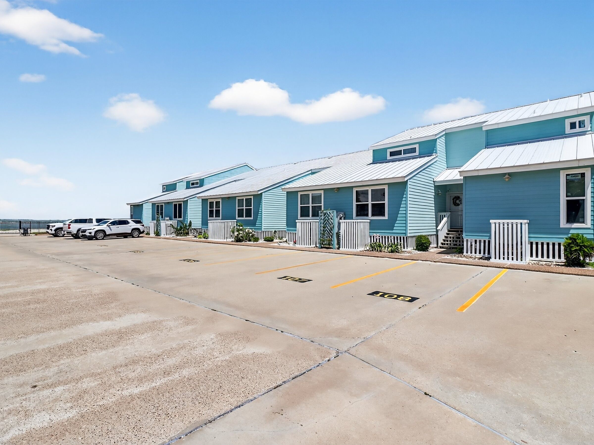 A row of light blue motel buildings with white picket fences and a parking lot in front.