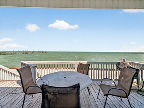 A deck with a table and chairs overlooking the ocean, a pier in the distance, and a clear sky. - Bayfront Kontiki 107 3 Bedroom Condo (Rockport)