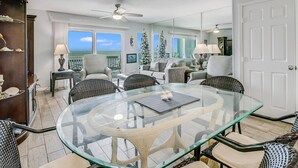 A spacious living room with a glass-top dining table, comfortable seating, a large window with a view, and a Christmas tree.