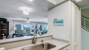 A kitchen with a stainless steel sink, white cabinets, and a ceiling fan.