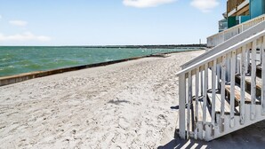A beach with a wooden walkway leading to a building with a balcony.