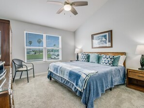 A bedroom with a bed, a chair, a ceiling fan, a window with blinds, and a framed picture on the wall. - Bayfront Kontiki 107 3 Bedroom Condo (Rockport)