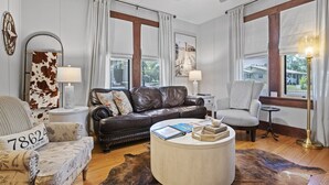 A spacious living room with a leather sofa, a round coffee table, and a patterned armchair. - 1929 Craftsman Charmer 2 Bedroom Home (Fredericksburg)
