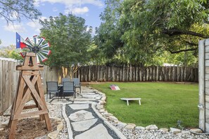 Un patio trasero con valla de madera, un molino, una mesa con sillas y una zona verde.