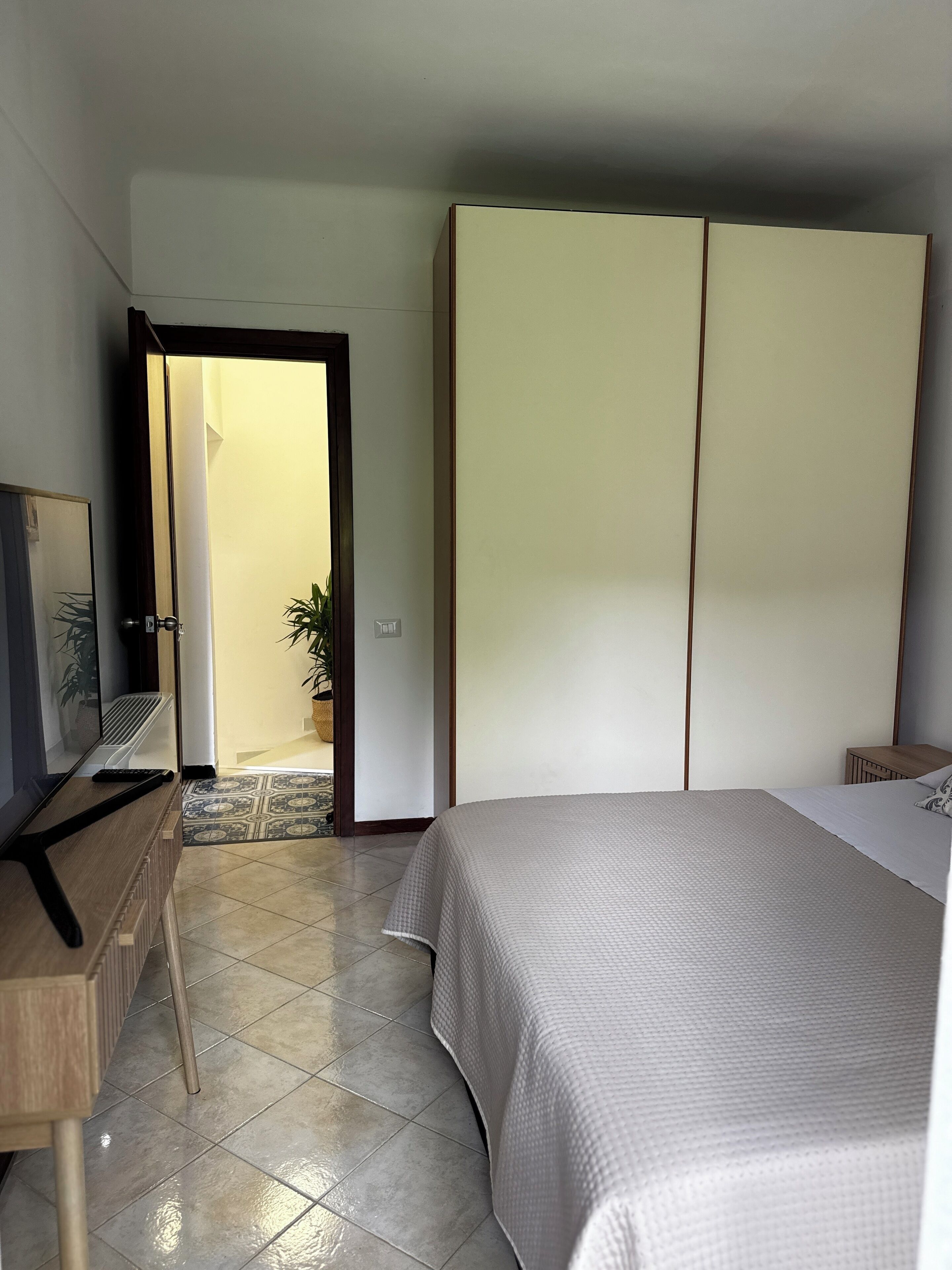 A bedroom with a bed, a wardrobe, a desk, and a television.