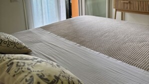 Une chambre à coucher avec un lit, un téléviseur posé sur un meuble et une fenêtre avec des stores.