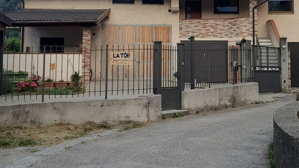 Un edificio de dos pisos con techo de tejas, entrada protegida por una reja y un camino de acceso a un estacionamiento.