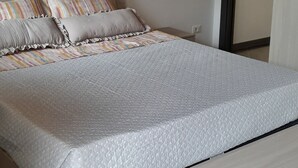 Un dormitorio con techo de madera, cama con colcha gris y suelo de baldosas grises.