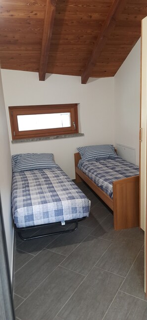 Ein kleines, schlichtes Zimmer mit zwei Einzelbetten, einem Fenster und einer Holzbalkendecke.