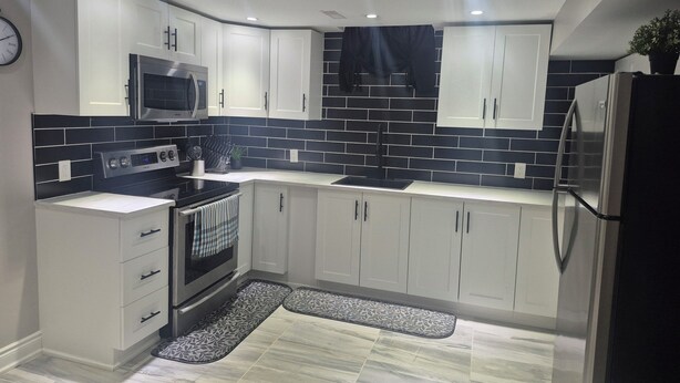 Una cocina moderna con armarios blancos, salpicadero blanco y negro, electrodomésticos de acero inoxidable y una alfombra estampada.