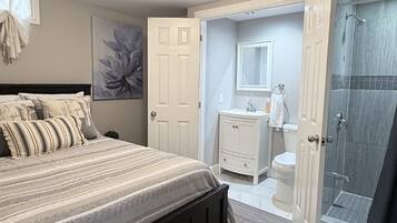 A bedroom with a bed, a bedside table, a dresser, a mirror, and a shower area.