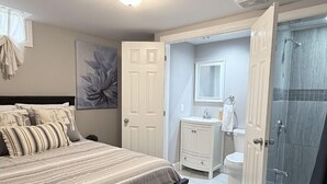 Un dormitorio con cama, un baño con ducha, y una puerta que da a otra habitación.