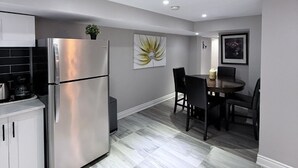 Una cocina moderna con un refrigerador de acero inoxidable, un comedor con mesa y sillas, y una pared gris con un cuadro de flores.