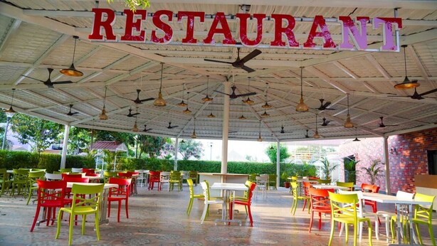 Un restaurante al aire libre con terraza cubierta, varias mesas y sillas, y ventiladores de techo.