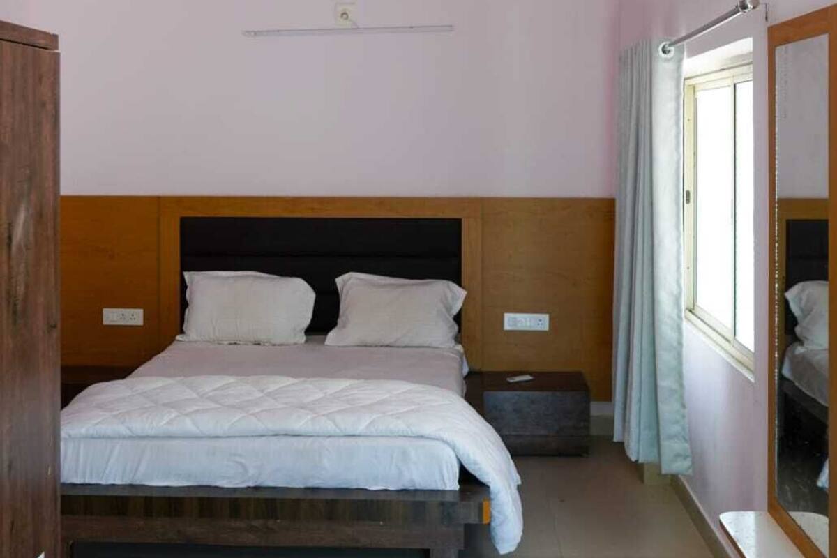 Quarto com cama, ventilador de teto, mesa de cabeceira e janela com cortinas.