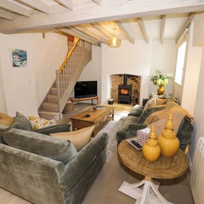 A living room with a sofa, a coffee table, a TV, a fireplace, and a staircase. - Charming 3-bedroom cottage in lovely Broadway with WiFi & Parking for 1 car. (Broadway)