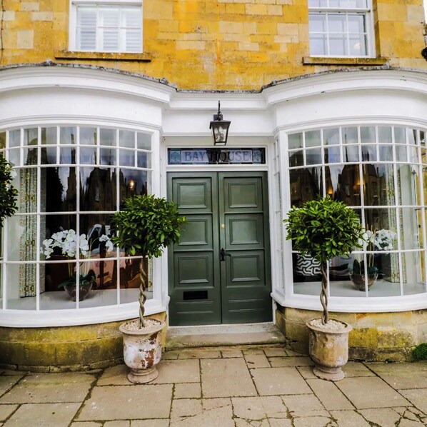 A corner bay window with a green door, potted plants, and a lamp above the door.