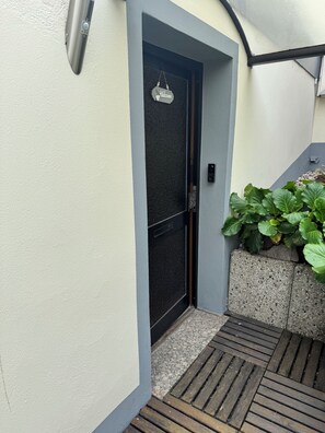 A modern entrance with a black door, a welcome sign, and a small garden area with plants. - Flick Apartment (Unknown)