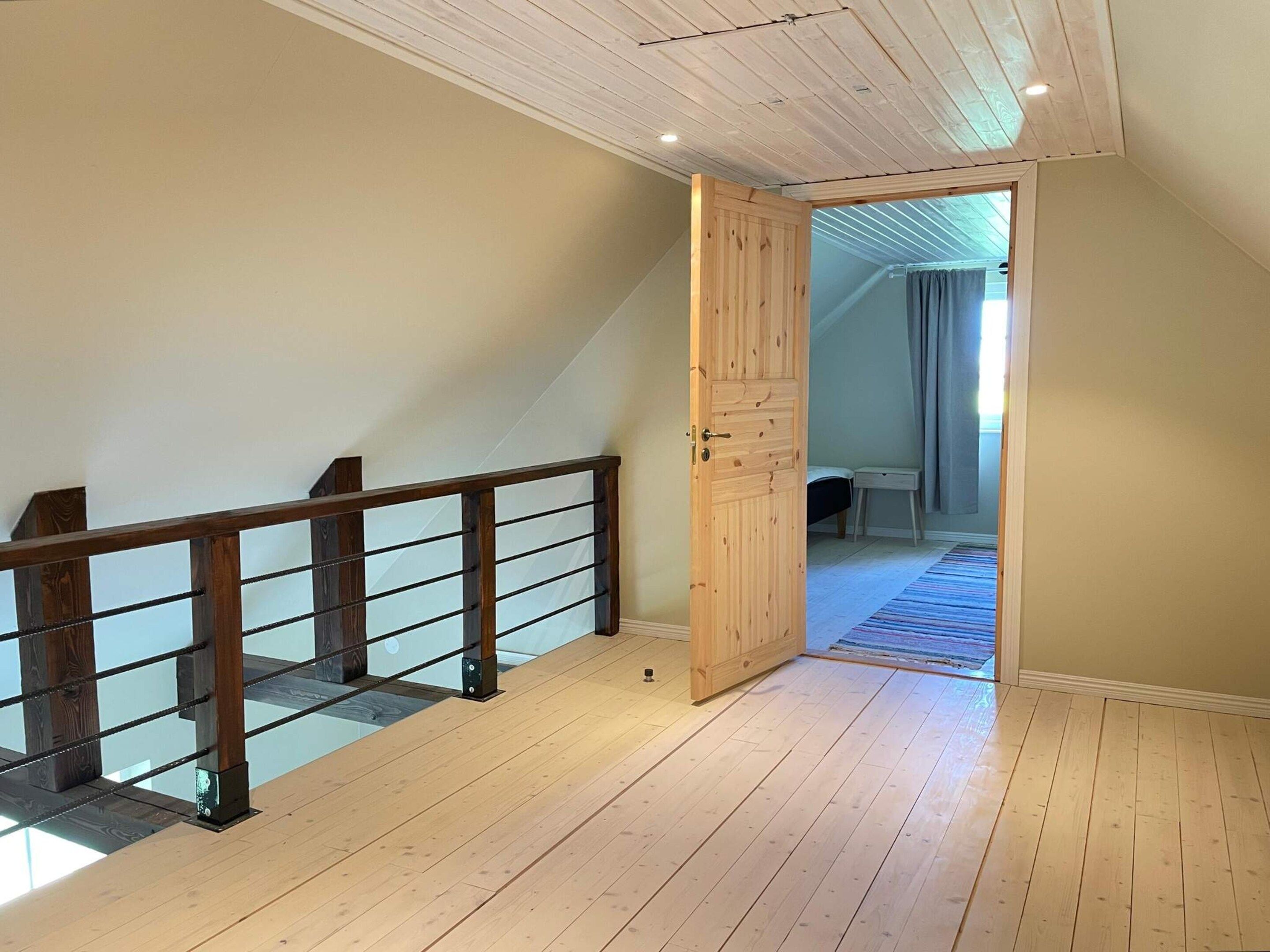 Una habitación con escalera de madera, una puerta que da a otra estancia y un banco a la vista.