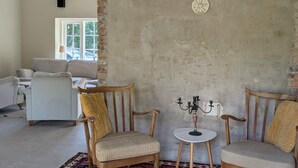 A room with a rustic brick wall, a round table with a candelabra, two wooden chairs, and a sofa in the background. - 5 Star Holiday Home in Hammenhog (Hammenhög)