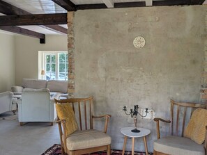 Une pièce avec un mur en briques au style rustique, une table ronde surmontée d’un chandelier et deux fauteuils rembourrés.