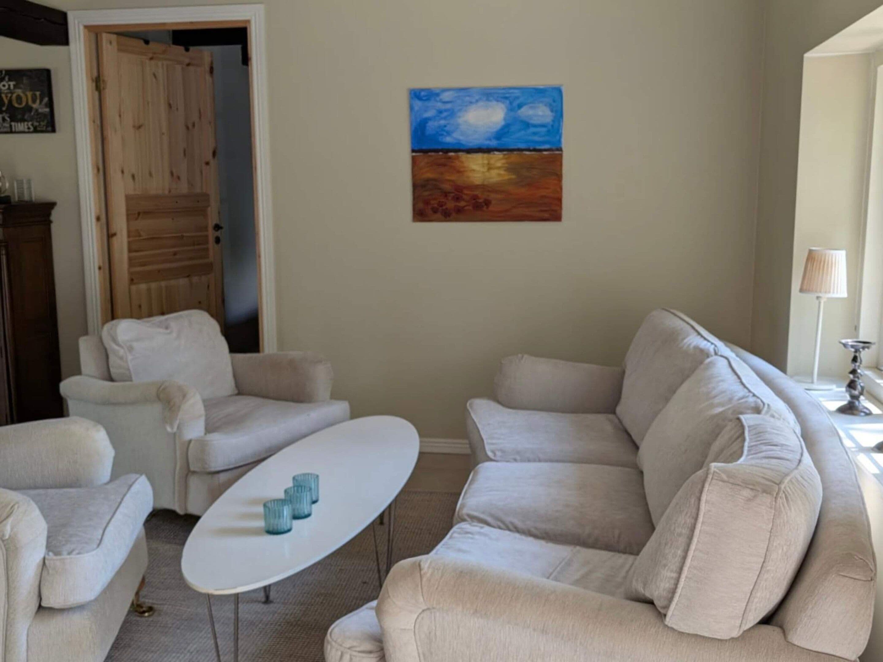 Una sala de estar con un sofá color beige, una mesa de centro blanca y un cuadro en la pared.