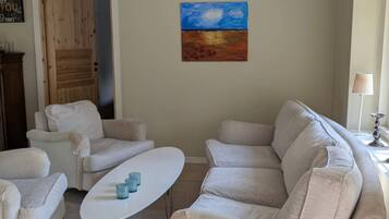 Una sala de estar con un sofá color beige, una mesa de centro blanca y un cuadro en la pared.