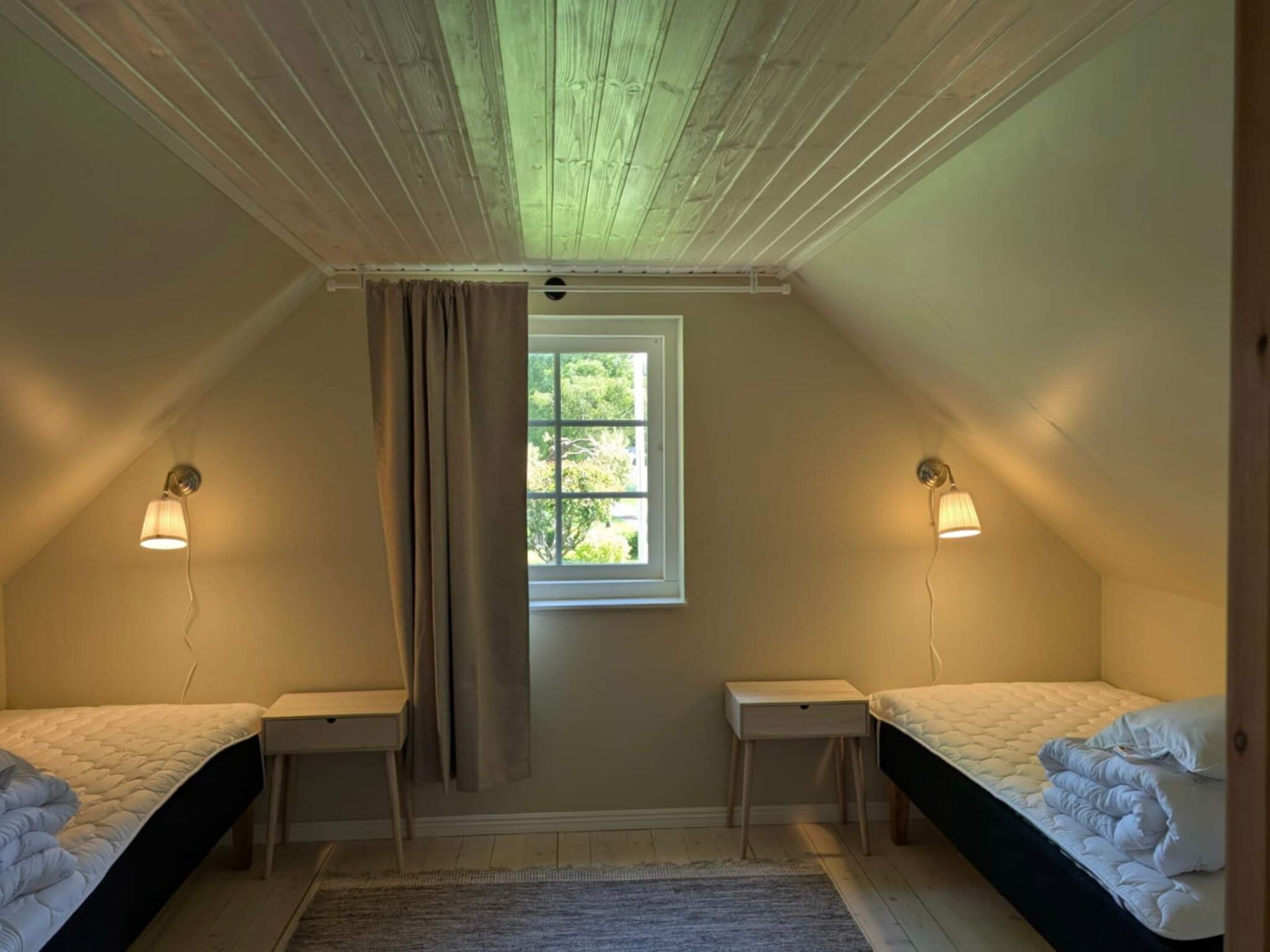 Un dormitorio pequeño y acogedor en el ático con dos camas individuales, una ventana y una lámpara en el techo.