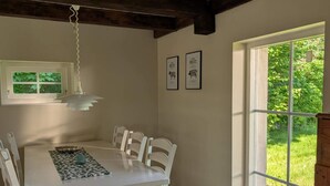 A dining area with a white table and chairs, a hanging light fixture, framed pictures on the wall, and a large window with a view of greenery. - 5 Star Holiday Home in Hammenhog (Hammenhög)