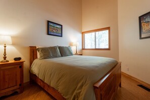 Une chambre à coucher avec un lit en bois, deux lampes de chevet, une fenêtre et un tableau encadré au mur.