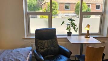 Una habitación con una cama, un sillón de cuero negro, una mesita con una lámpara y una planta en maceta.