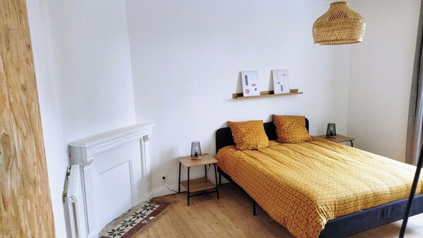 A bedroom with a bed, a bedside table, a nightstand, a wall-mounted shelf, and a hanging light fixture. - Large Family Home (Scaër)