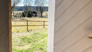 A view through a partially open door of a building with a wooden fence in the foreground and a rural landscape with trees and a house in the background. - 4 Star Holiday Home in Sandhem (Mullsjö)