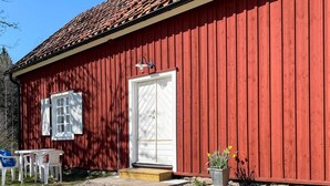 A red wooden building with a tiled roof, a white door, and a small porch with a bench. - 4 Star Holiday Home in Sandhem (Mullsjö)