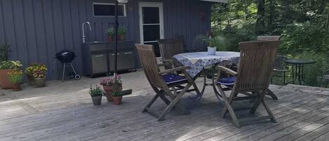 A wooden deck with a table and chairs, a barbecue grill, and a shed with a window and door.