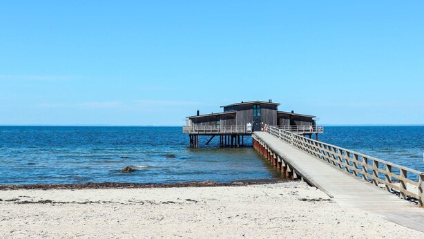 Une jetée menant à une structure en bois dotée d’une terrasse, qui s’avance sur une mer calme.
