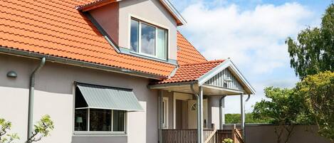 A two-story house with a red-tiled roof, a covered porch, and a patio with outdoor furniture.