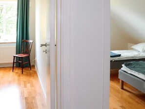 A room with a wooden floor, a bed with white bedding, a chair, and a window with curtains. - 4 Star Holiday Home in Forslov (Förslöv)