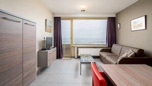 Moderni hotellihuone, jossa on parveke, sohva, ruokapöytä ja televisio.